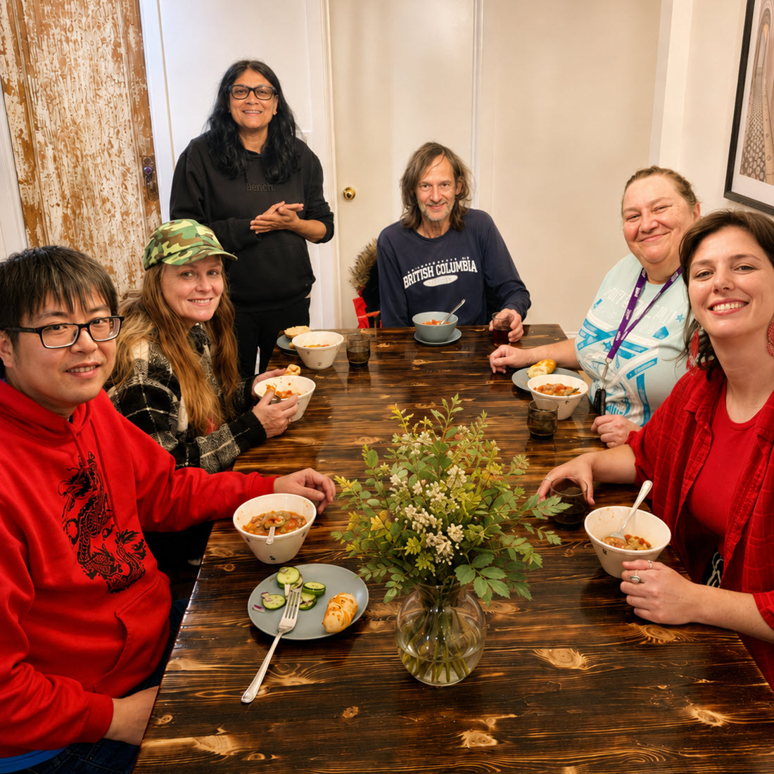 Neighbours gathered around a wooden table sharing a meal together